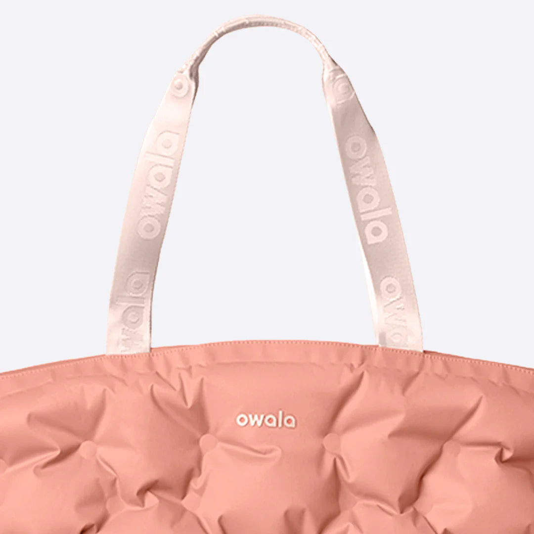 Close-up of the Owala Cloud Insulated Tote in Rosewood, peach pink pillowed body with cream owala-tape handles featuring repeating Owala logo and cream Owala logo on the body