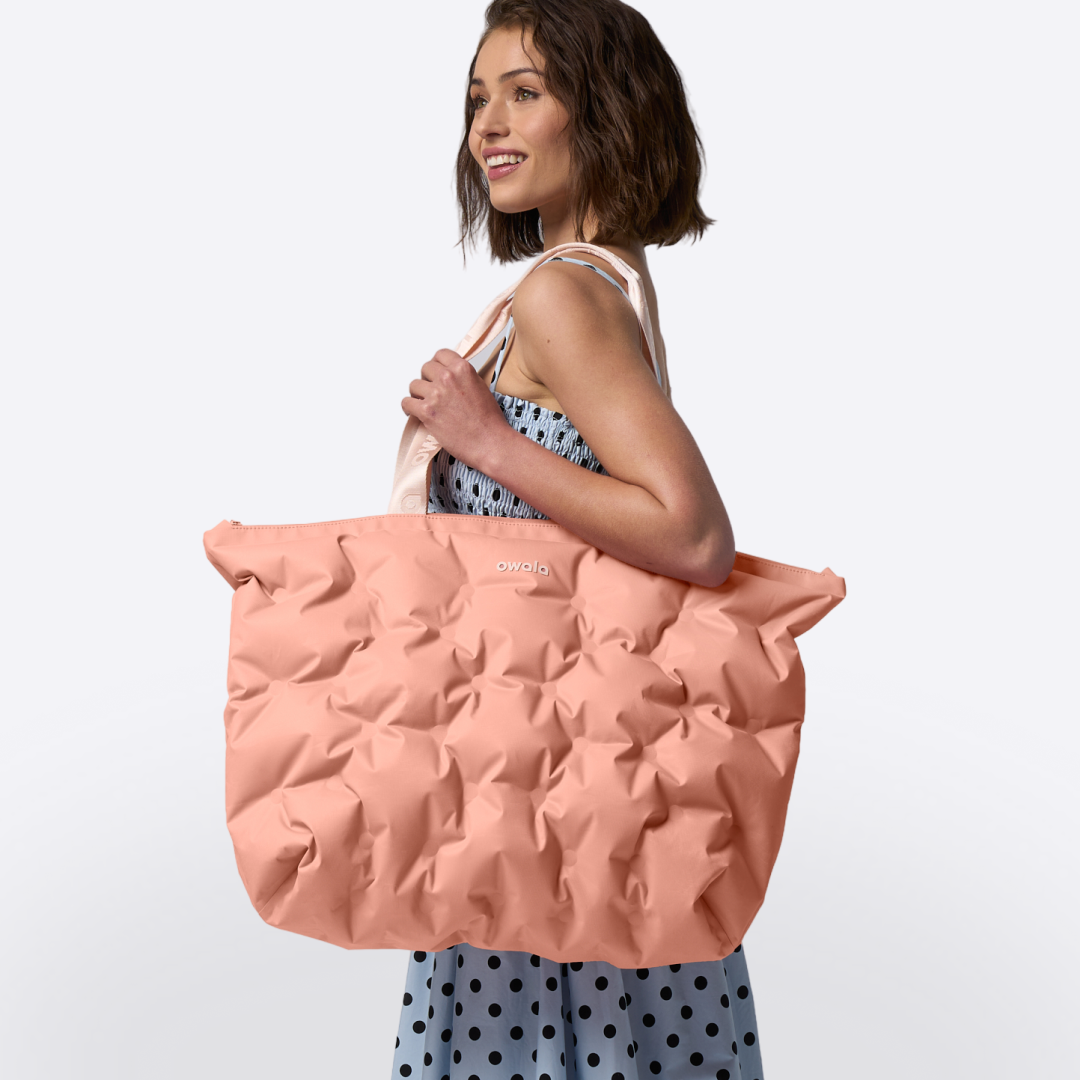 Model carrying the Owala Cloud Insulated Tote in Rosewood on her shoulder, peach pink pillowed body with cream owala-tape handles