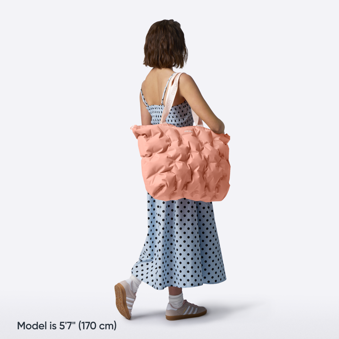 Model walking with the Owala Cloud Insulated Tote in Rosewood slung over her shoulder, peach pink pillowed body with cream owala-tape handles
